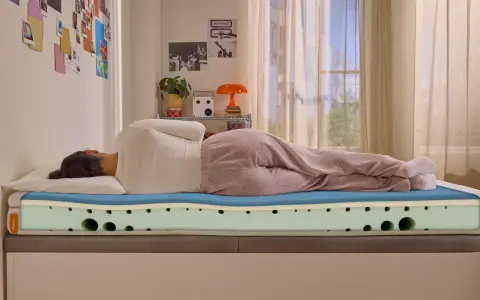 Frau liegt auf einer Emma Matratze, die zu hart erscheint. Die Schichten der Matratze sind sichtbar.