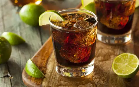 Orzeźwiający drink: bacardi z czymś ciemnym i lodem, ozdobiony plasterkami limonki.