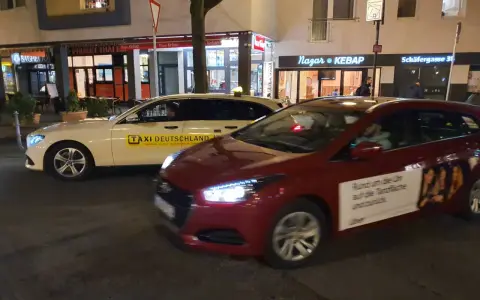 Ein weißes Taxi und ein rotes Auto mit Uber-Werbung stehen nebeneinander. Der Unterschied über Taxi ist die moderne Alternative.