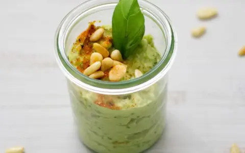 Cremiges Avocado Pesto in einem Glas, garniert mit Pinienkernen, Basilikum und Paprikapulver. Ein Genuss für jeden Tag!
