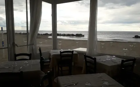 Tavoli apparecchiati in un ristorante con vista sulla spiaggia di Misano durante la bassa marea.