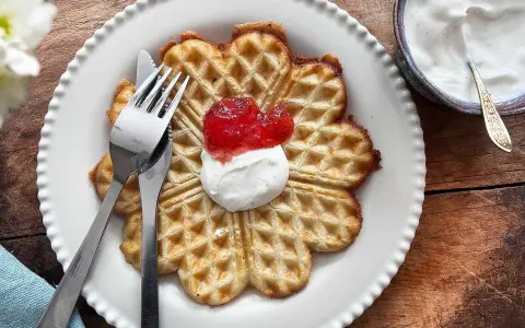 En vacker, hjärtformad våffla, perfekt för en fika. Dessa glutenfria våfflor serveras med vispad grädde och sylt.