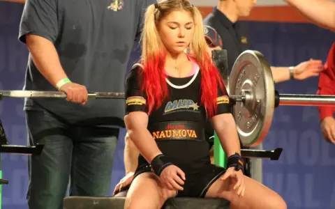 Młoda sportsmenka z rudymi pasemkami włosów przygotowuje się do wyciskania na klatę. Czy to będzie nowy rekord świata?