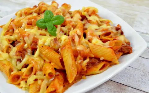 Penne z sosem pomidorowym i kawałkami pikantnego chorizo, zapieczone pod ciągnącym się serem, ozdobione listkiem bazylii.