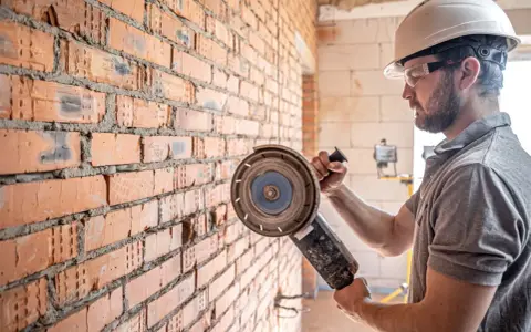 Obrero con casco y gafas protectoras listo para cortar pared con radial.