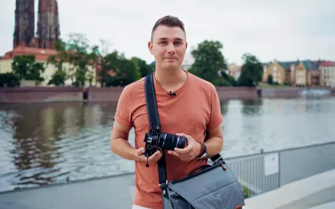 Mężczyzna z aparatem w rękach, na tle rzeki i zabytkowych budynków. Jakość 4k jaka to rozdzielczość, idealna do uchwycenia detali.