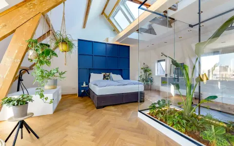 Mansarde da sogno con letto blu, piante sospese e un giardino interno in vetro. Travi a vista e lucernari creano un'atmosfera unica.