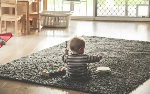 Liten bebis sitter på en matta och leker med en xylofon och en tamburin. En perfekt start på en checklista bebis för musikaliska äventyr.
