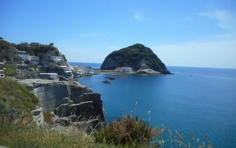 Scogliere a picco sul mare blu, case bianche aggrappate alla costa e un isolotto verde. Un paesaggio che ispira frasi su Ischia.
