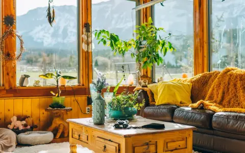 Un acogedor **salón estilo natural** con sofá de cuero, manta naranja, plantas y vistas a la montaña.