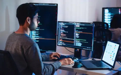 Programista pracuje nad projektem test ai, pisząc kod na wielu monitorach.