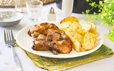 Contramuslos de pollo jugosos y dorados con patatas asadas en un plato blanco.