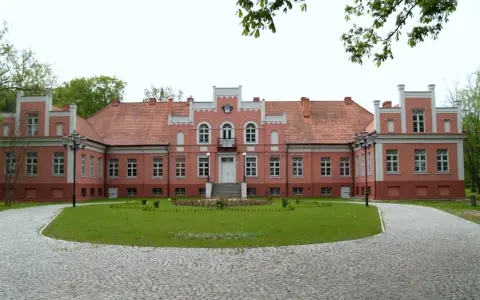 Pałac Przebendowskich w Wejherowie, różowy, z czerwonym dachem, otoczony zielenią i brukowanymi alejkami.