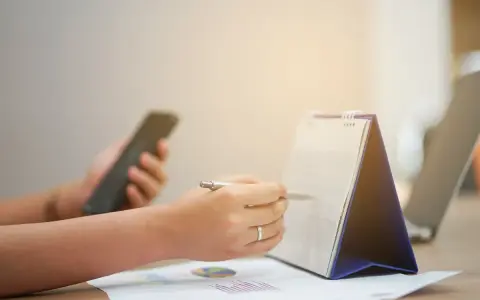 Ręce planują zadania na kalendarzu, trzymając telefon. Zapewnia to ciągłość pracy i organizację dnia.