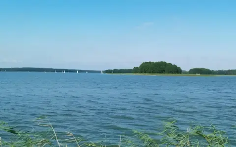Spokojne jezioro Jagodne, gdzie żaglówki suną po wodzie, a w głębinach czają się ryby.