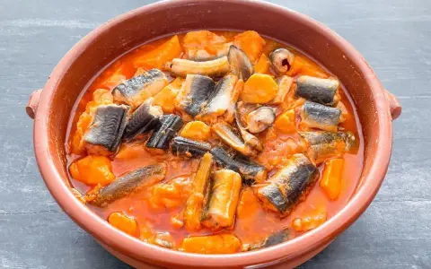 Un sabroso all i pebre en cazuela de barro, con trozos de anguila y patatas en una salsa rojiza.
