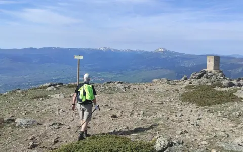 Senderista camina hacia el **puerto de Navafría**, con un mojón y montañas nevadas al fondo.