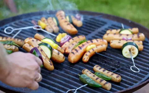 Grilla korv med grönsaker på en kolgrill. Röken stiger från den saftiga maten.