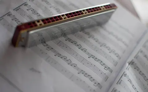 Harmonijka ustna spoczywa na kartach z nutami, gotowa do zagrania melodii.