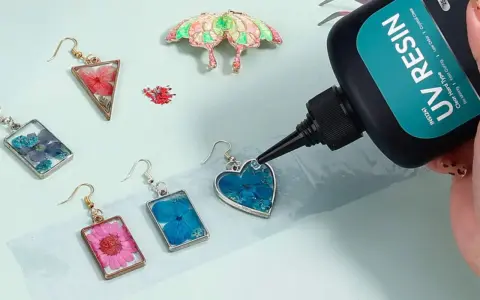 A hand applies UV resin to a heart-shaped earring with blue flowers, demonstrating how UV resin works to create beautiful jewelry.