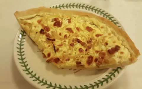 Part de quiche lorraine, une des spécialités lorraines, sur une assiette décorée de feuilles vertes.