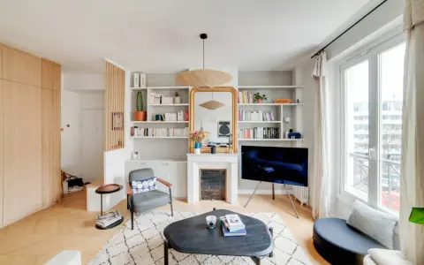 Aménagement entrée ouverte avec rangements boisés, fauteuil, cheminée décorative et étagères remplies de livres.