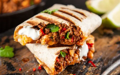 Pyszne burrito przepis: soczyste mięso mielone, ciecierzyca, papryczka chili i śmietana, podane na desce.