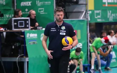 Trener Michał Piwowarczyk z piłką siatkową w dłoni, gotowy do akcji na boisku.