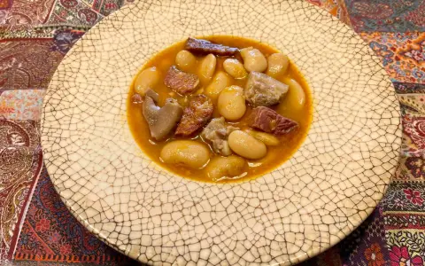 Plato de judiones de la granja receta tradicional, con trozos de tocino y carne en un caldo sabroso.