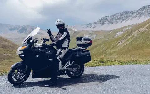 Motocyklista w kasku pozdrawia na tle gór. Przełęcz Stelvio zamknięta, ale widoki zapierają dech w piersiach.