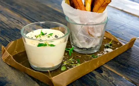 En krämig creme fraiche sås med örter serveras bredvid en glasbehållare med krispiga pommes frites på ett rustikt träbord.