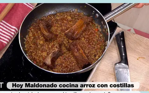 Un delicioso arroz con costillas se cocina en una sartén, con trozos de carne jugosa y arroz dorado.