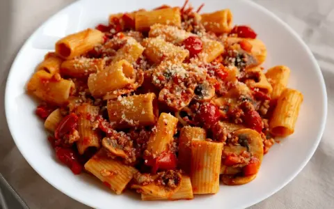 Pyszny makaron z sosem pomidorowym, grzybami i parmezanem na białym talerzu.