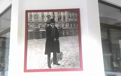 Ritratto di Franz Kafka, figura iconica che ci fa chiedere chi era Kafka, in piedi su un selciato con un edificio sullo sfondo.