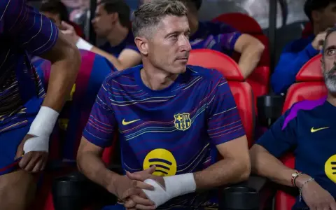 Robert Lewandowski w meczu FC Barcelona – Valencia CF, siedzi na ławce z bandażem na ręce, skupiony na grze.