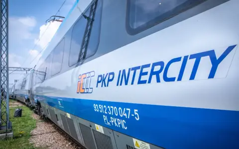 Pociąg PKP Intercity z niebieskim pasem i logo, na tle nieba.