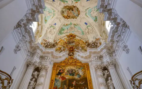 Magnifique plafond orné de fresques et de sculptures, typique du style baroque, avec un tableau doré au centre.