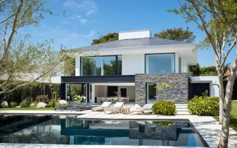 Une maison moderne simple avec piscine, terrasse et mobilier de jardin. Le soleil brille sur cette demeure épurée.