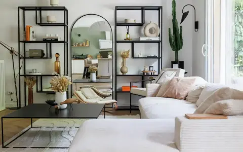 Soggiorno con divano bianco, librerie nere, specchio ad arco e cactus. Un'oasi di pace in stile casa minimal.