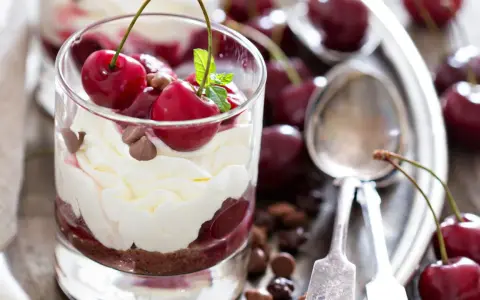 Delicioso postre con capas de crema batida, bizcocho de chocolate y cerezas frescas, coronado con más cerezas y trocitos de chocolate.