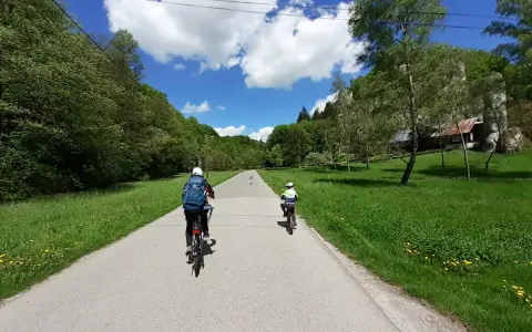 Dwie osoby na rowerach przemierzają malownicze **ojcowskie park narodowy trasy rowerowe**. Słoneczny dzień, zieleń i chmury na niebie.