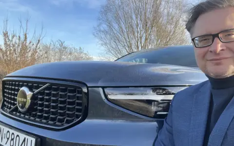 Mężczyzna w okularach i garniturze pozuje do zdjęcia z przodu Volvo XC40. Czy są jakieś wady tego modelu?