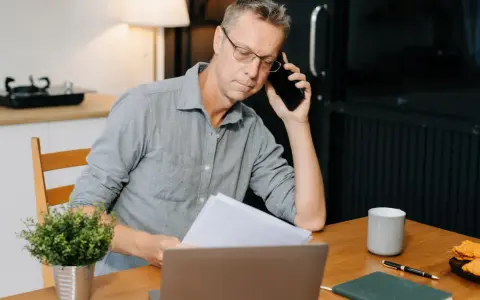 Mann am Telefon, der Dokumente prüft. Frustriert, weil die Kfz-Versicherung nicht zahlt.