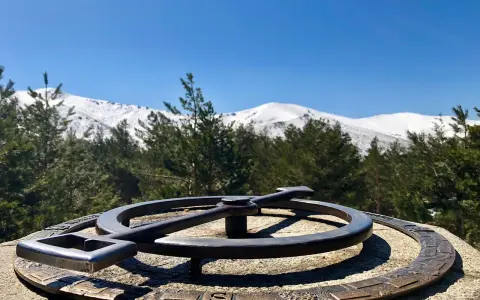 Un mirador de la gitana con un compás de bronce y montañas nevadas al fondo.