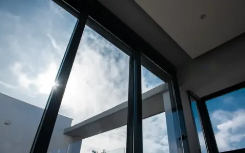 El sol brilla a través del vidrio guardian, iluminando un cielo azul con nubes blancas.