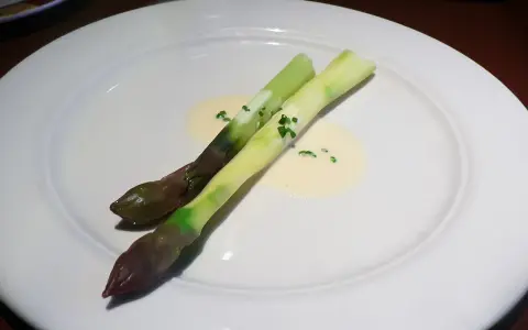 Zwei Spargelstangen auf einem Teller, serviert mit einer cremigen beurre blanc Sauce und gehackten Kräutern.