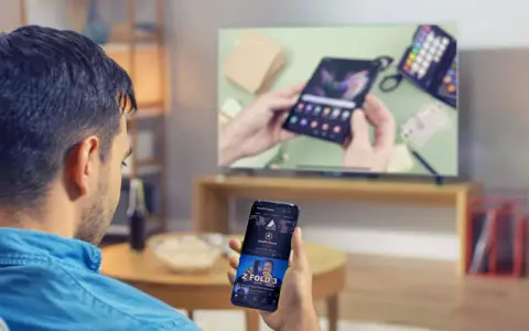 Mann verbindet sein Handy mit dem Fernseher, um ein Video anzusehen. Auf dem Handy ist ein YouTube-Video zu sehen.