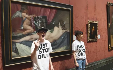 Dwie osoby w koszulkach "Just Stop Oil" stoją przed obrazem "Wenus z lustrem", który został uszkodzony.