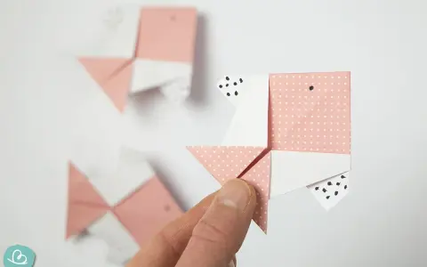Hand hält Origami-Fisch. Mehrere rosa und weiße Papierfische, die gefaltet wurden, sind im Hintergrund zu sehen.