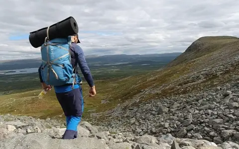 Vandrare med ryggsäck och liggunderlag på väg nerför en stenig fjällsida. En perfekt packlista vandring för äventyret.
